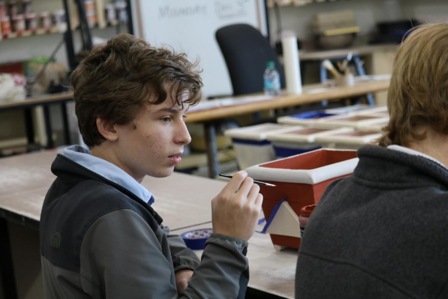 Joseph Powell ‘20 watches as Sterling Smith ‘20 shows him how to get glaze in hard to reach places.  “I can’t wait to see my piece after it has been fired off.  I scored often and deep so I know my piece will be sturdy when it comes out of the kiln” Powell said.  